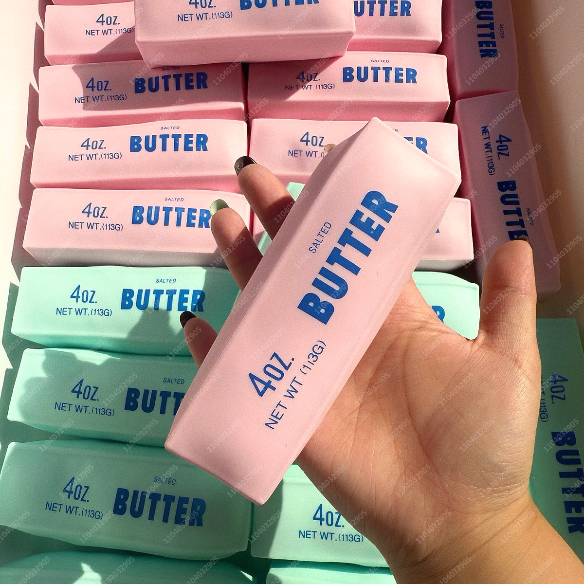Eine Hand hält ein rosa Butter-Fidget-Spielzeug mit bunten Butterblöcken im Hintergrund.