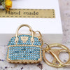 A gold-toned handbag keychain decorated with blue crystal rhinestones, set against a white background.