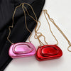 A pair of mini gold metal clutch bags with long chains are displayed against a black fabric background.