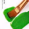 A gold-handled flat brush with green paint is shown on a white background.