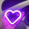 A hand holds a glowing neon heart light illuminating the interior of a car window.