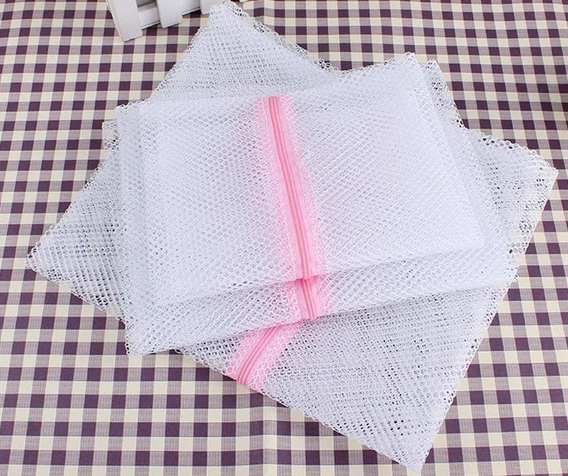 A stack of white mesh laundry bags with pink zippers resting on a checkered cloth.