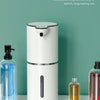 A white touchless automatic soap dispenser with a black pump and an interchangeable replaceable soap bottle on a glass surfac