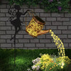 A vintage solar watering can garden light with a shepherd's hook is shown pouring water onto plants in a garden setting.