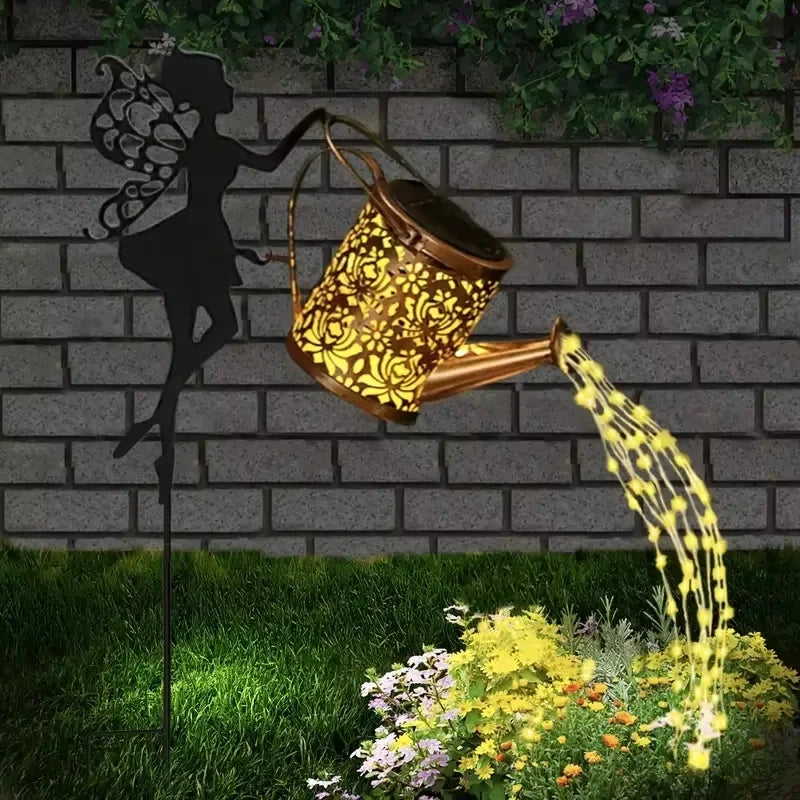 A vintage solar watering can garden light with a shepherd's hook is shown pouring water onto plants in a garden setting.