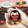 A handmade knitted penguin doll with a heart tag is held in a person's hand against a festive background.