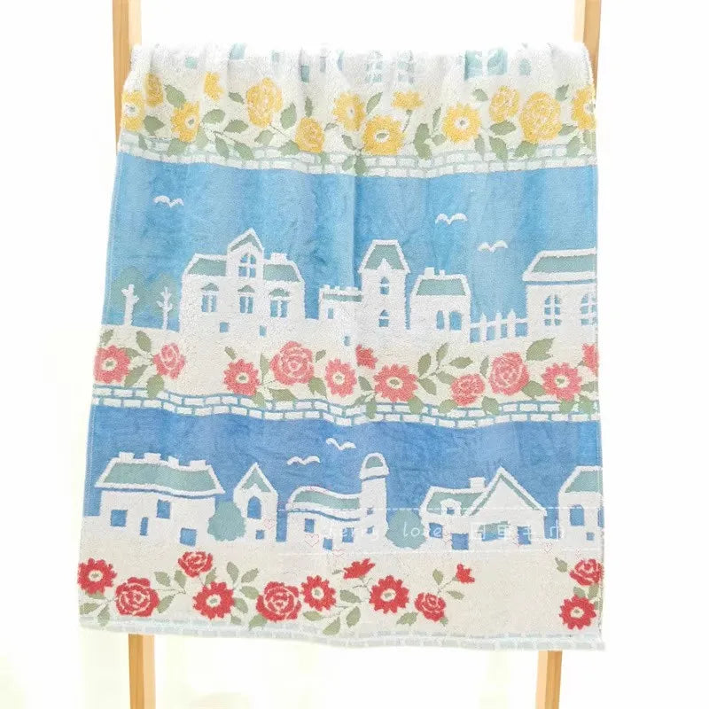 A light blue towel featuring a white embroidered cartoon cityscape with pink and green floral accents.