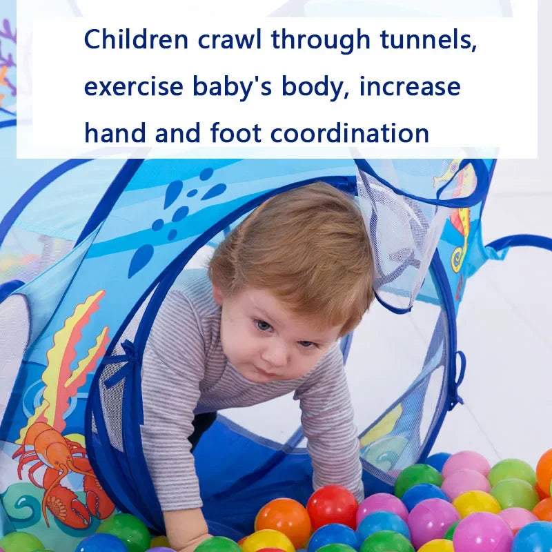 A toddler crawls through a blue ball pit play tent with an attached tunnel, surrounded by colorful balls.