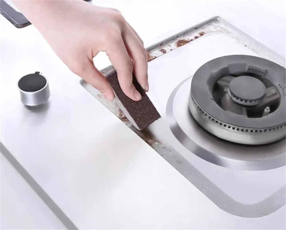 A hand is using a dark cleaning sponge to wipe a surface on an Emery cleaning sponge.