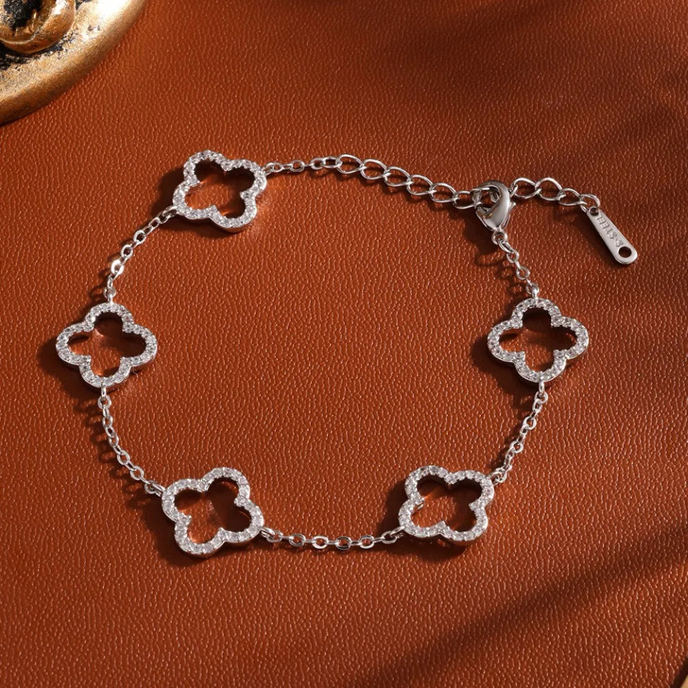 A silver stainless steel four-leaf clover bracelet with cubic zirconia displayed on a brown surface.