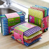 A collection of colorful double-sided kitchen scouring sponges in various patterns and colors stacked on a wooden surface.