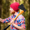 A man wearing a red beanie and plaid shirt holds a wooden axe with a black blade cover.