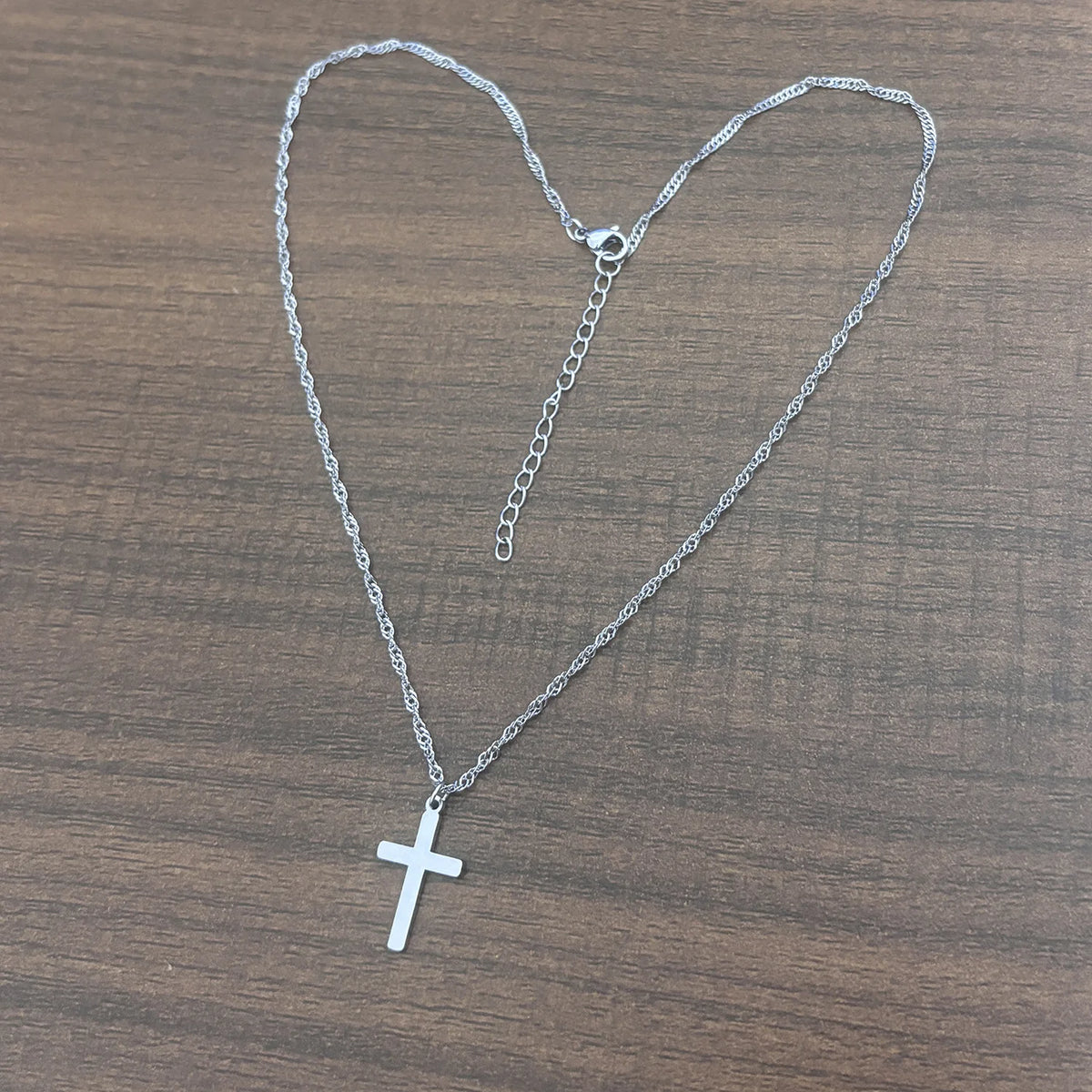 Collier en croix argenté avec une chaîne, exposé sur une surface en bois.