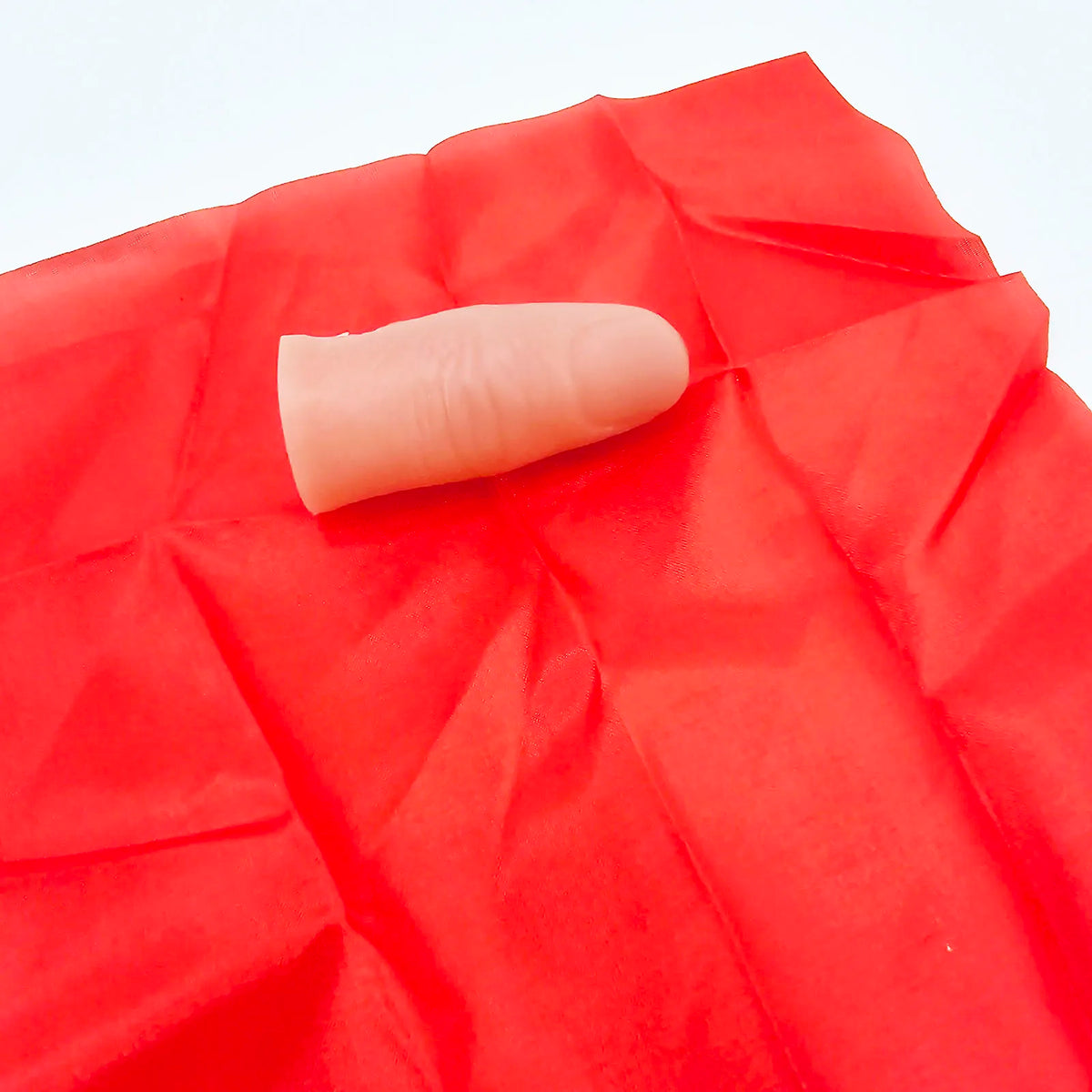 A pale pink thumb tip product is visible on a bright red, crinkled silk background.