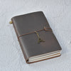 A brown leather refillable journal with a brass-colored leather tie and stacked white paper pages.