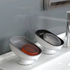 A white soap dish with a leaf-shaped suction cup holder and an orange soap dish sitting on a white bathroom sink.