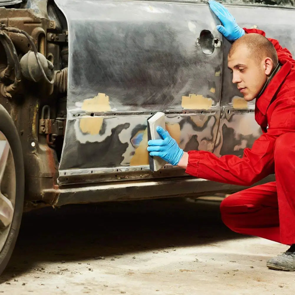 A person in a red jumpsuit is using a tool to access the interior of a vehicle, working on a metal panel.