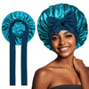 A woman models a blue satin silk sleep bonnet tied in a bow, showing the fabric and style.