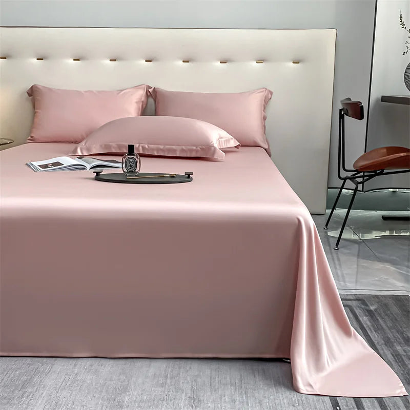 A pink luxury bamboo flat sheet is displayed on a bed with matching pillows and a watch.