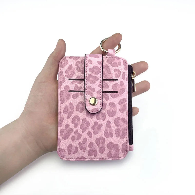A hand holds a pink leopard print PU leather card holder with a coin pocket and keychain.