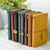A row of handcrafted genuine leather refillable journals in various muted colors lined up next to a green plant.
