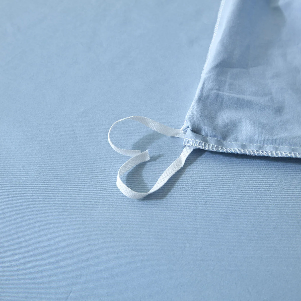Light blue quilted duvet cover set with white ties lying on a light blue surface.