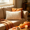 A cozy living room scene featuring an orange throw blanket and a cream embroidered plush pillow on a sofa.
