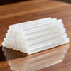 A row of clear, dual-size hot glue stick refills arranged in a neat rectangular shape on a wooden surface.