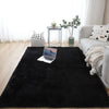 A black extra large Nordic fur rug placed on a light wood floor in a bright room with a sofa and plants.