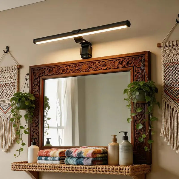 A wooden framed mirror hangs above a woven shelf displaying various glass bottles and green plants.