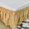 A beige adjustable elastic bed skirt with ruffled tiers covering the edge of a white mattress.