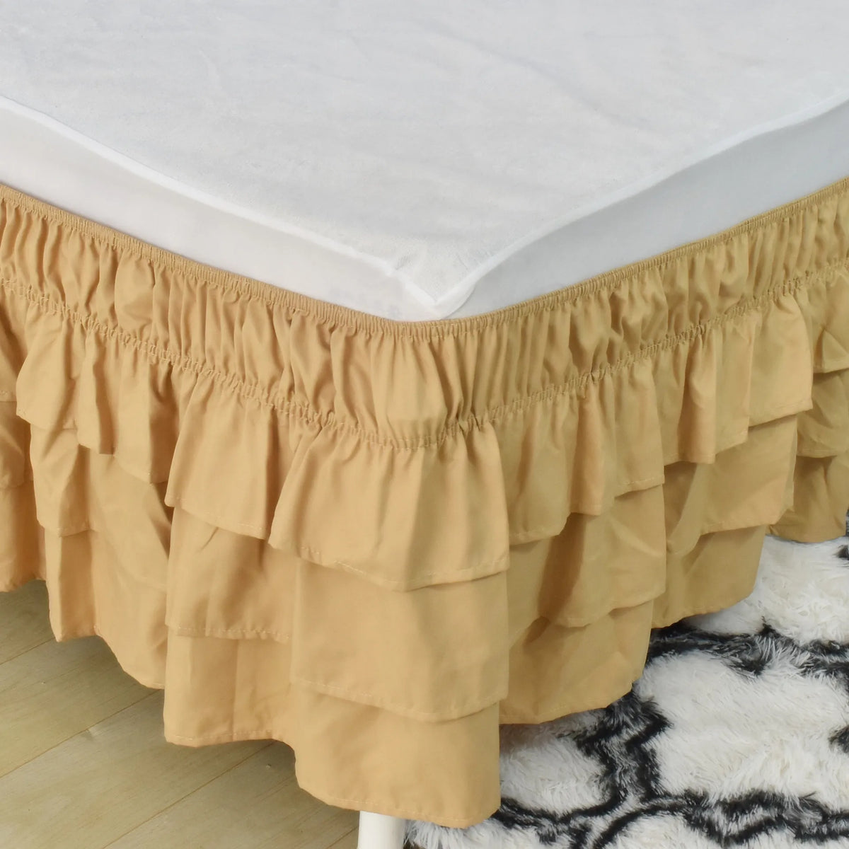 A beige adjustable elastic bed skirt with ruffled tiers covering the edge of a white mattress.