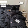 A set of black duvet covers and pillowcases with rose embroidery and lace details displayed on a bed.