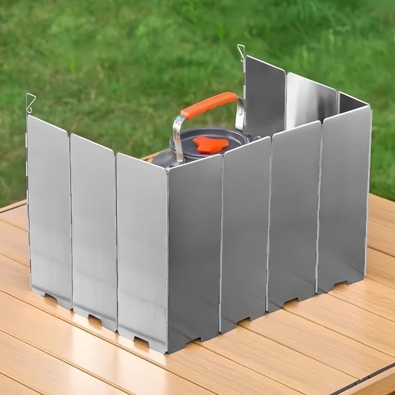 Silver aluminum camping stove with an orange handle and windscreen resting on a wooden surface.