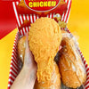 Eine Hand hält ein realistisches Spielzeug, das eine frittierte Hähnchenkeule simuliert, in einer rot-weißen Box.