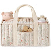 A beige floral diaper organizer bag with multiple compartments and a pink bear charm.