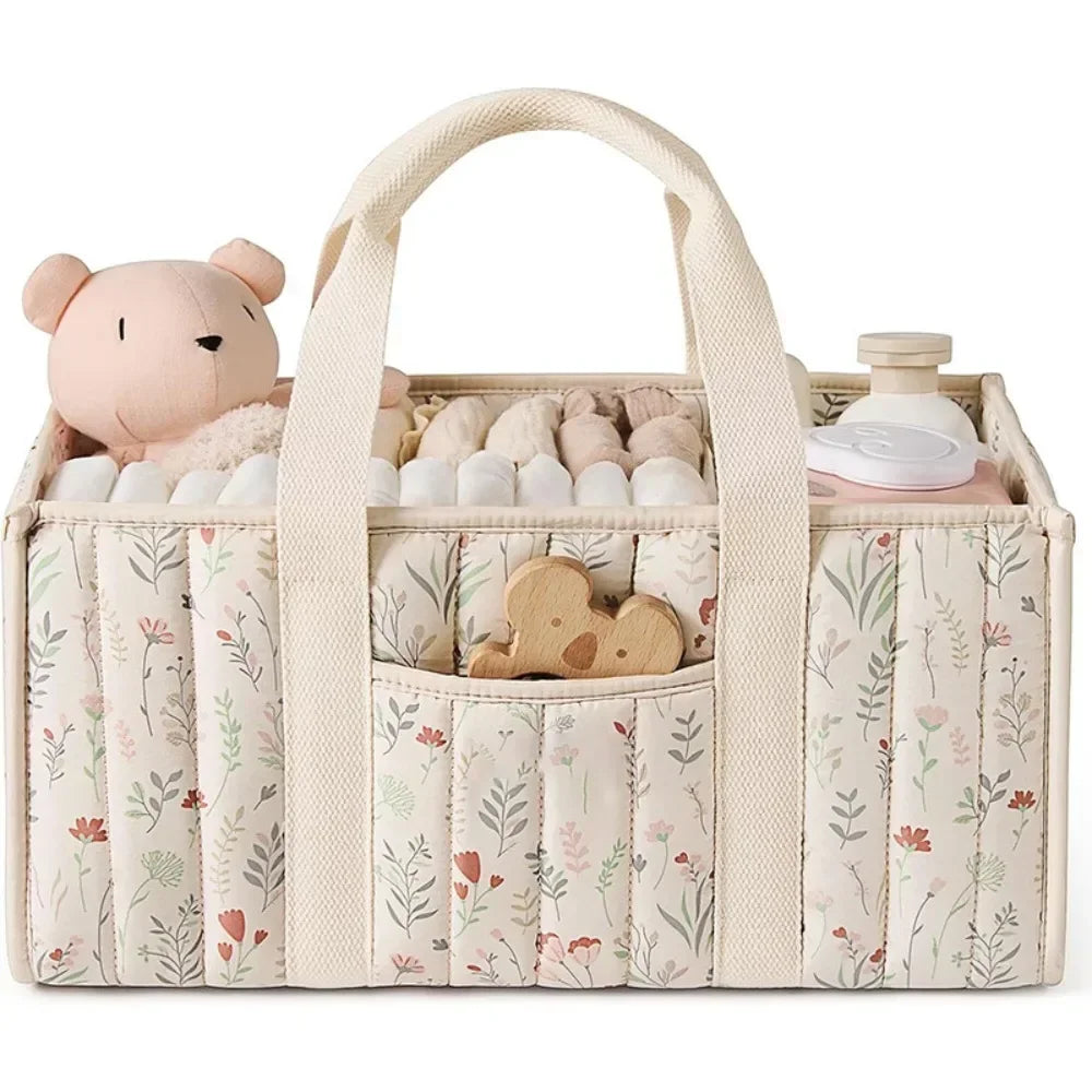A beige floral diaper organizer bag with multiple compartments and a pink bear charm.