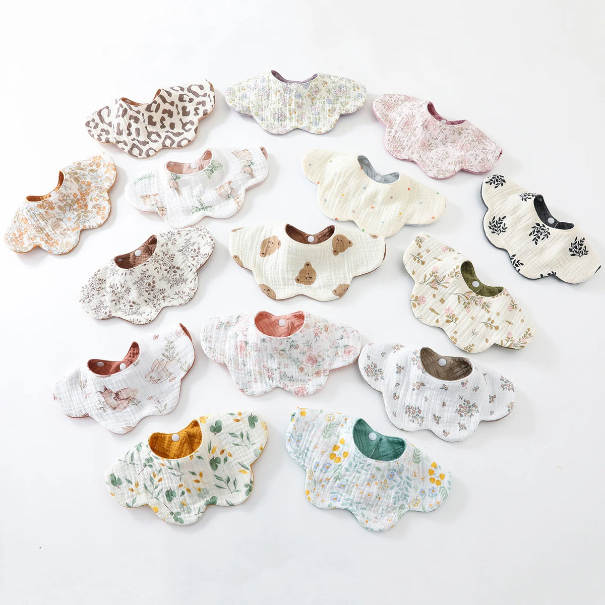 A collection of various patterned cotton baby feeding bibs in neutral tones and floral designs.