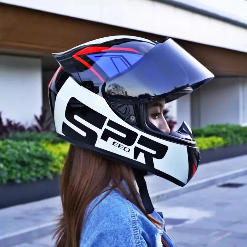 A woman wearing a black and white retro full-face motorcycle helmet with blue accents, standing outdoors.