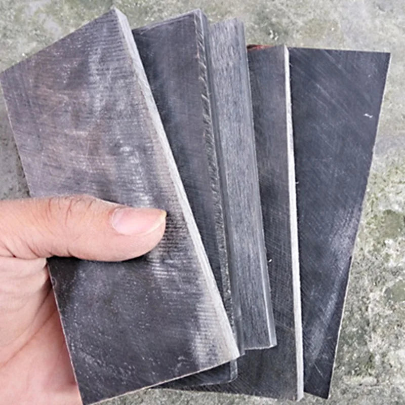 Two pieces of black buffalo horn knife handle scales are shown angled against a gray background.