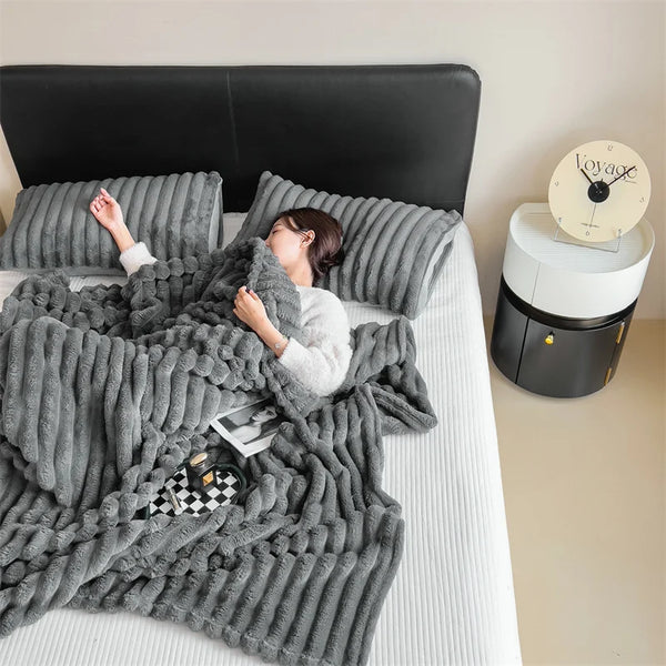 Una mujer relajándose en una cama cubierta con una manta gruesa de invierno gris y una cabecera negra.