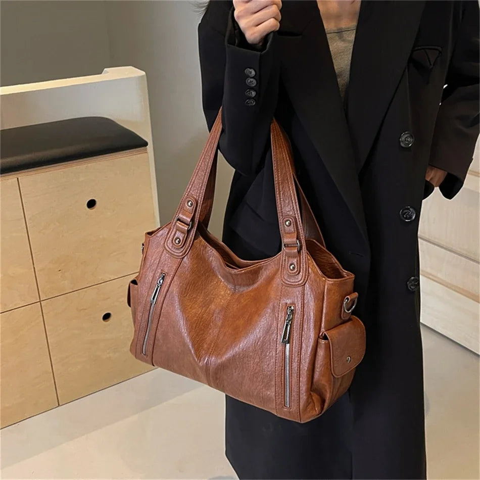 A close-up of a brown vintage leather tote bag with multiple pockets being held by a person wearing a black coat.