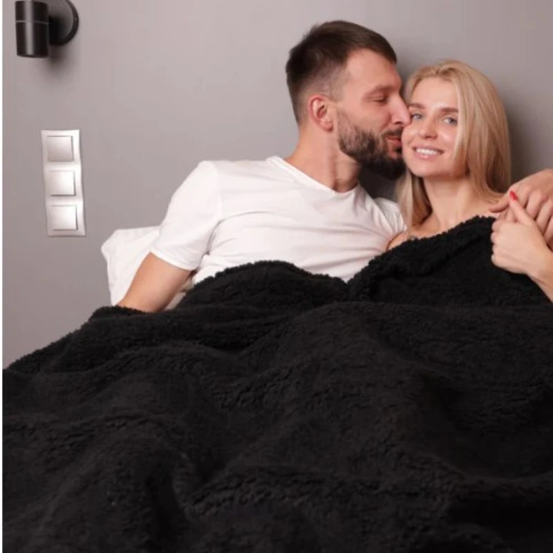 A couple embracing while wrapped in a black cozy waterproof throw blanket.