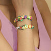 A wrist is adorned with a bracelet made of assorted polymer clay beads shaped like summer fruits for jewelry making.