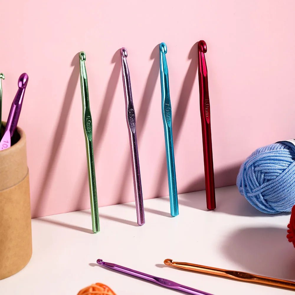 A collection of colorful Tunisian crochet hooks, including green, purple, and red, displayed against a pink background.