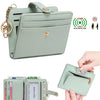 A light mint green bi-fold wallet with a leather strap and gold hardware, shown alongside a credit card.