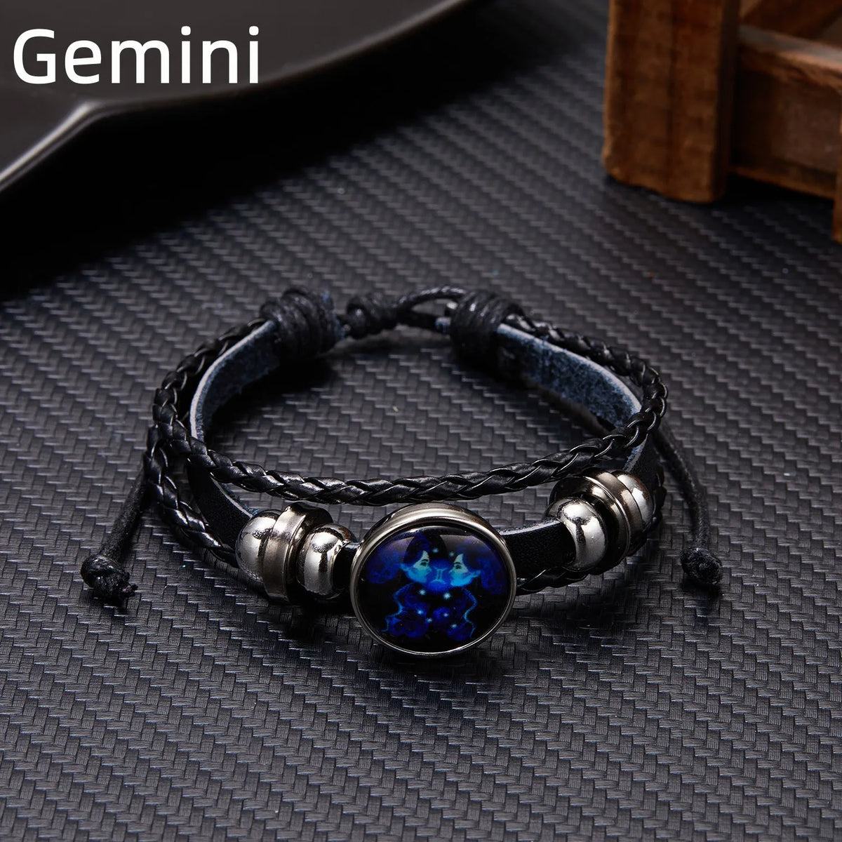 A black leather wrap bracelet featuring a glowing blue zodiac sign charm on a dark textured surface.