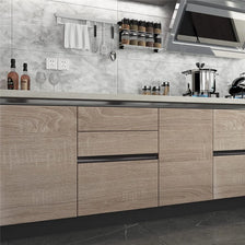 A modern kitchen featuring light wood grain cabinetry, stainless steel appliances, and a gray tiled backsplash.