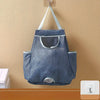 A gray mesh garbage bag holder is mounted on a wall with white hooks.
