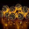 A close-up of glowing yellow Moroccan ball string lights reflecting on a dark surface.